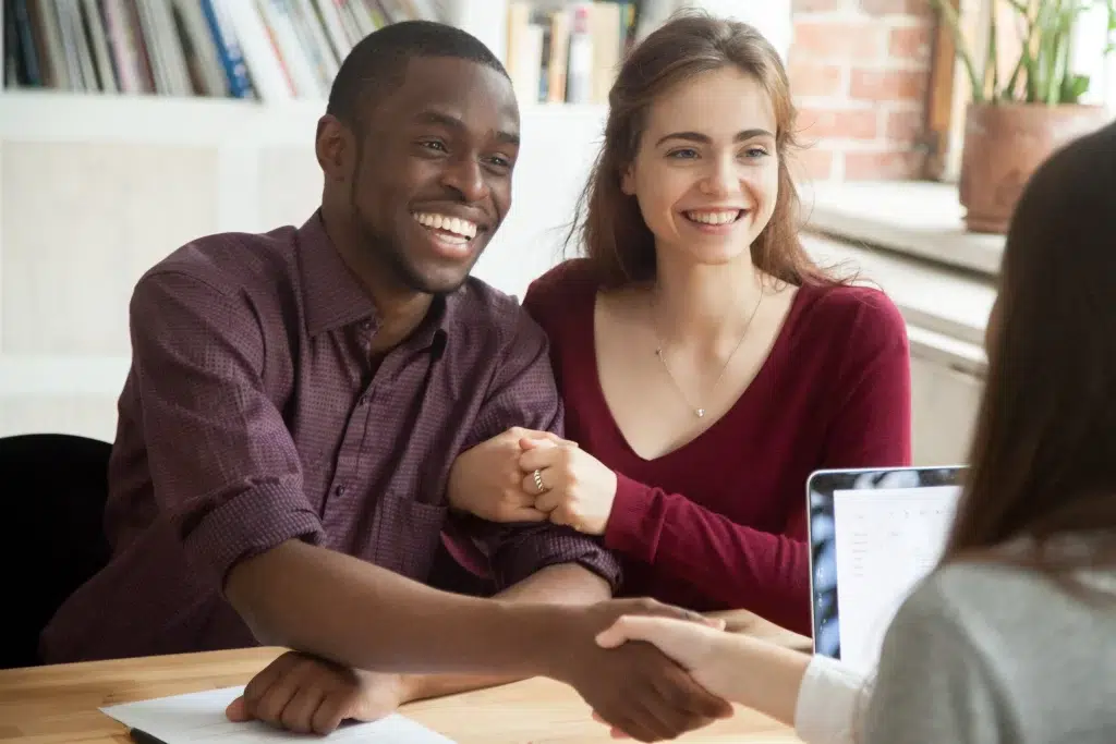 Smiling couple shakes hands with businesswoman.